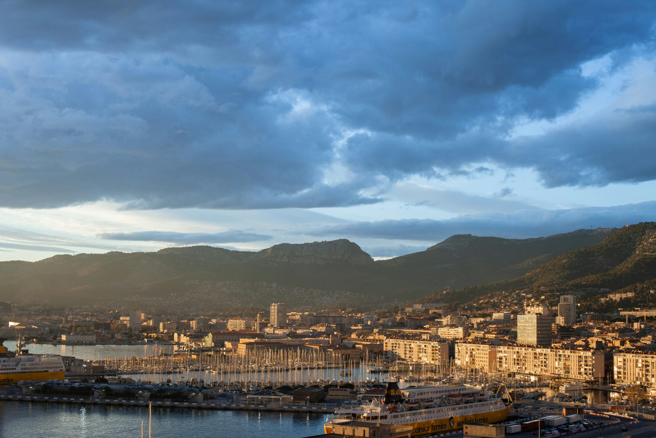 Consultant-seo-Toulon Photo du port de Toulon au coucher du soleil avec les montagnes en arrière-plan, illustrant les services d’un consultant SEO basé à Toulon.